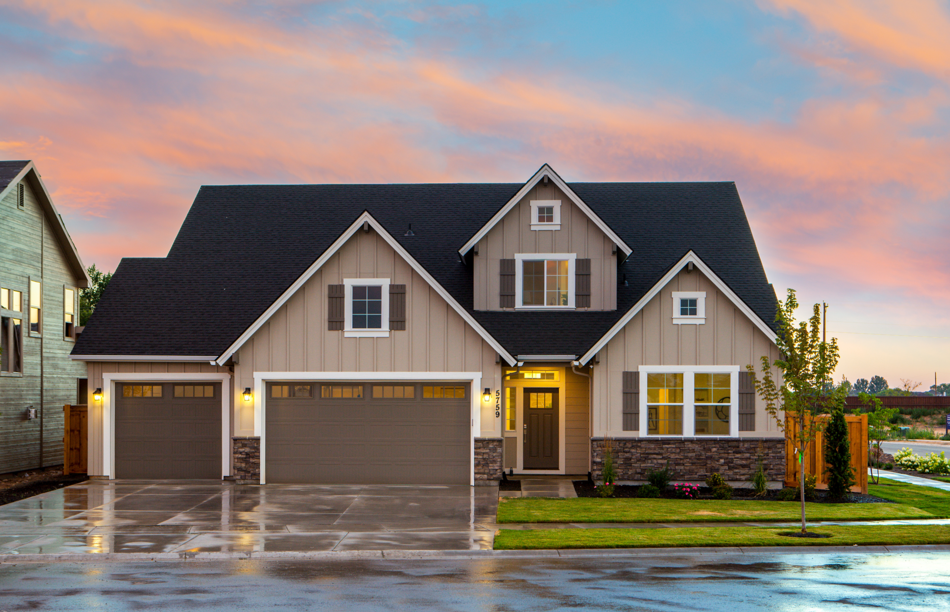 A large house with two garages and a sunset in the background.