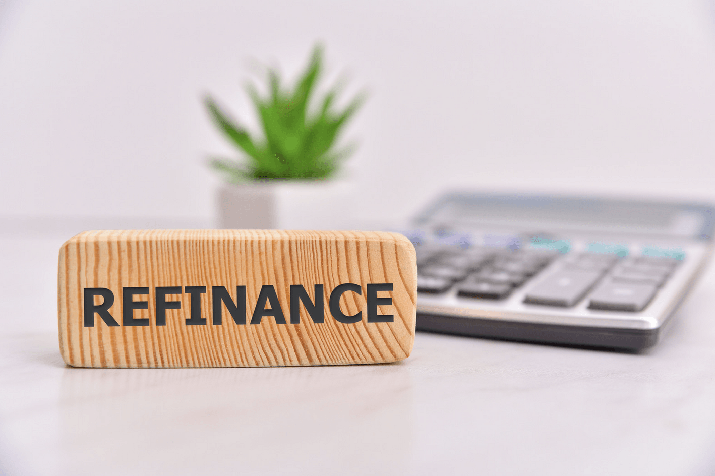 A wooden block with the word refinance written on it is sitting on a table next to a calculator.