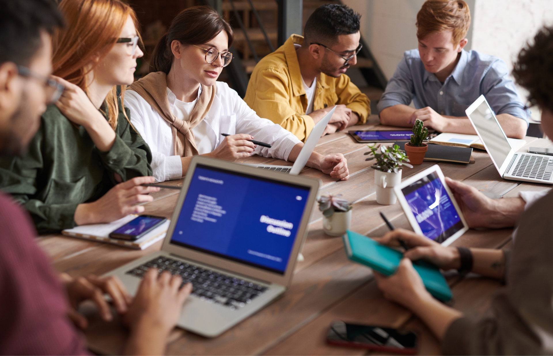A group of people are sitting around a table with laptops and tablets.