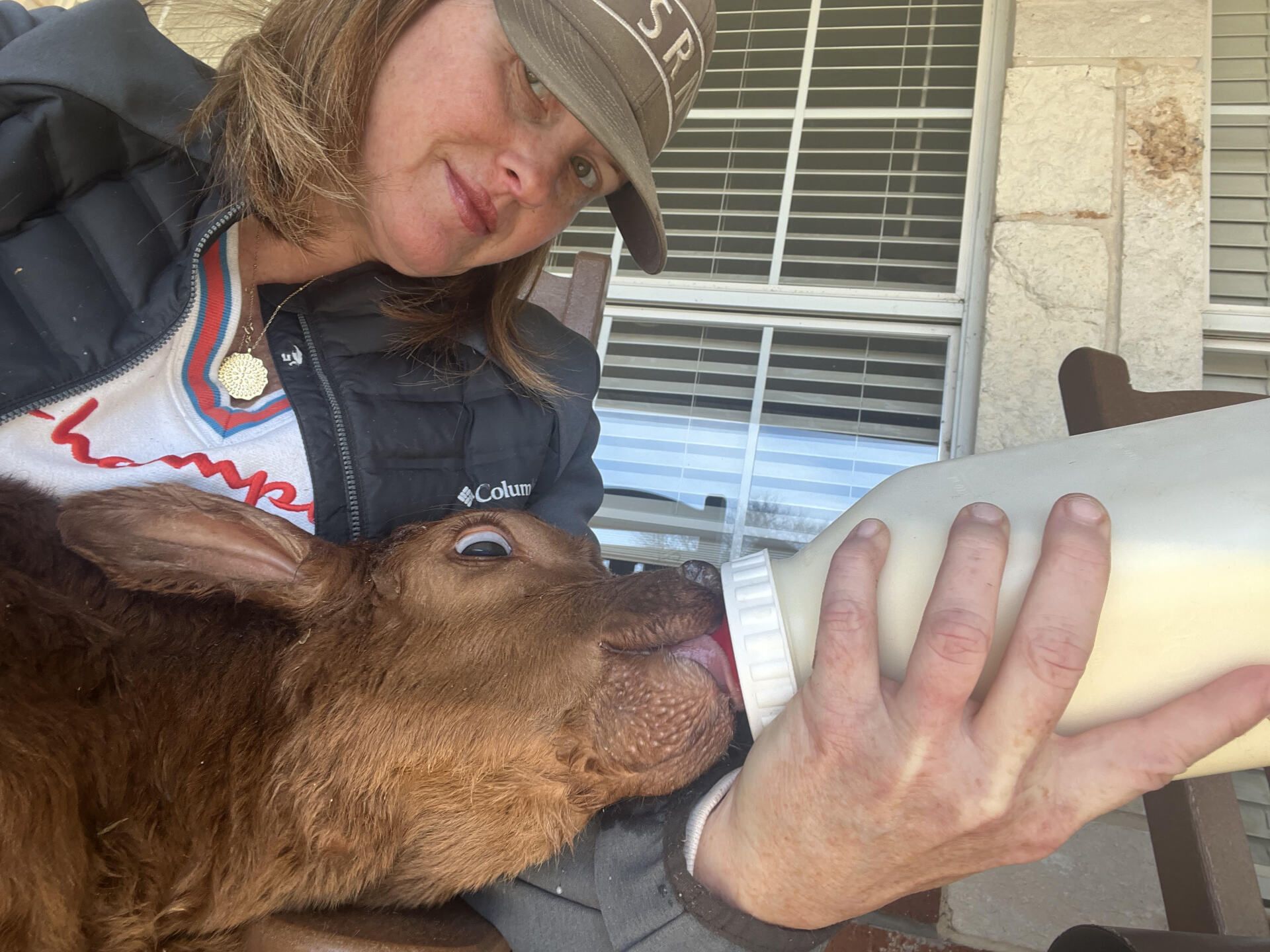 A woman is feeding a baby goat from a bottle
