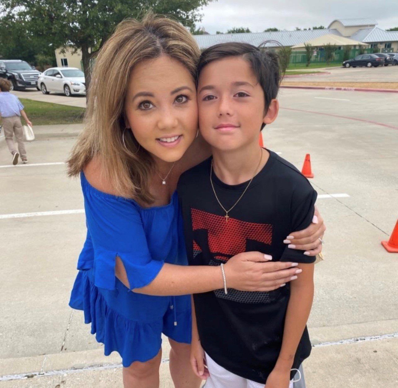 A woman in a blue dress is hugging a boy in a black shirt with the letter t on it