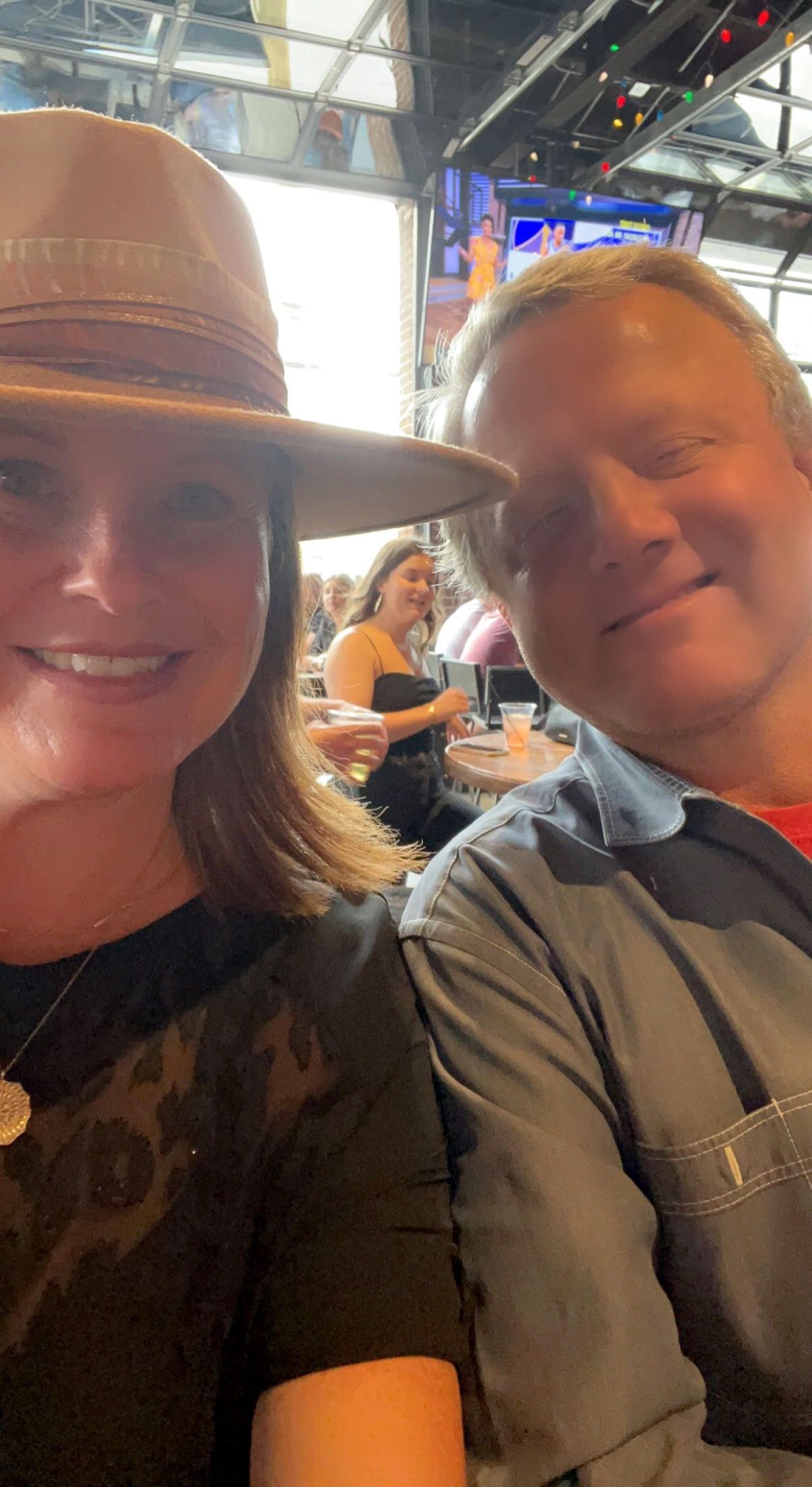 A man and a woman are posing for a picture in a restaurant . the woman is wearing a hat.