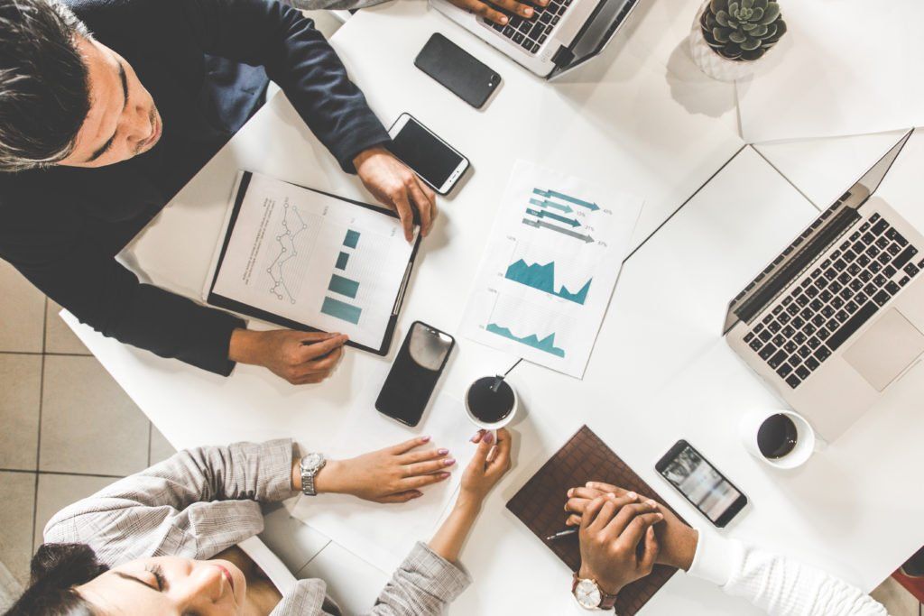 A group of people are sitting at a table with laptops and phones.