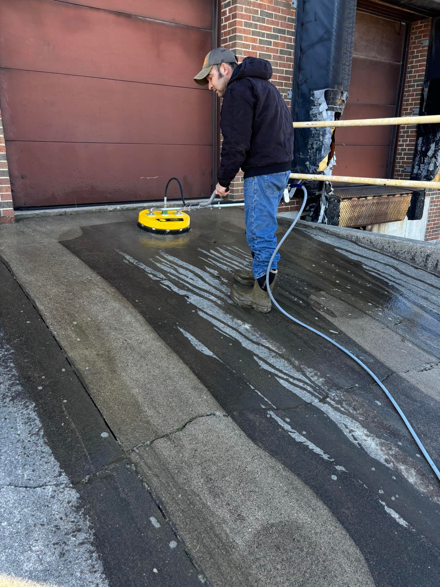 A man is cleaning the sidewalk with a yellow machine.