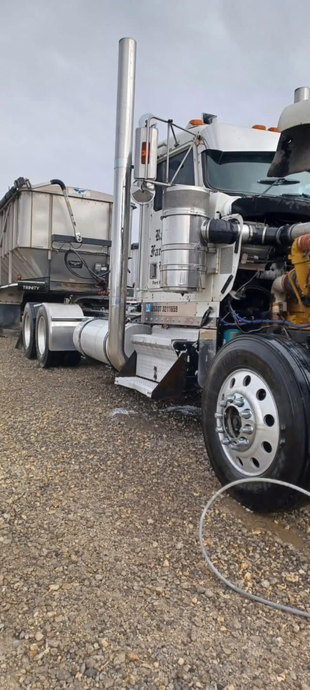 A semi truck with its hood open is parked in a gravel lot.