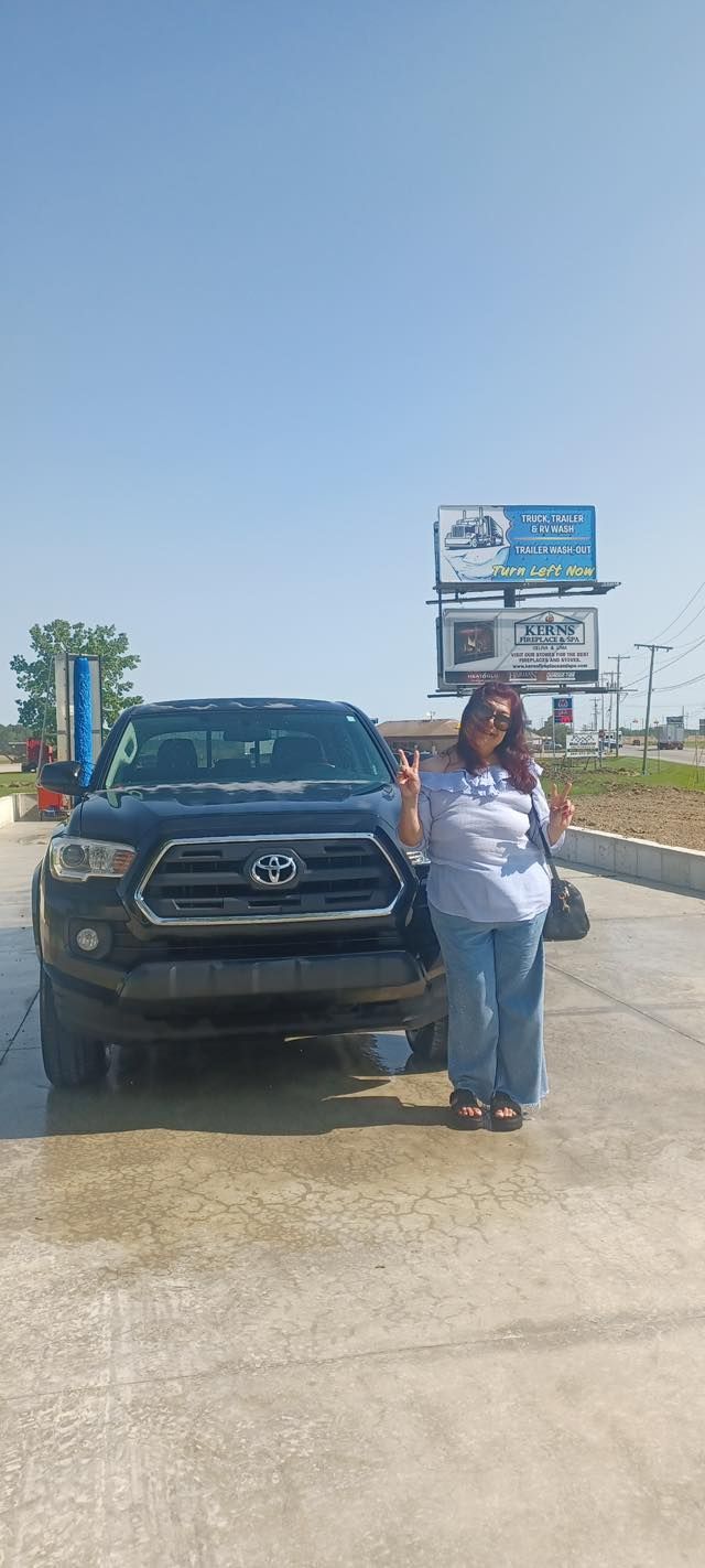 A woman is standing in front of a black truck.