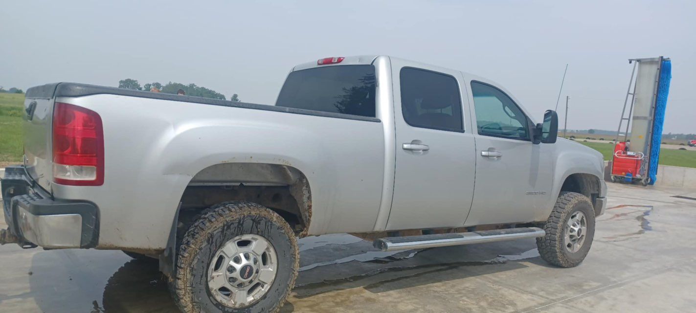 A silver pickup truck is parked on the side of a dirt road.