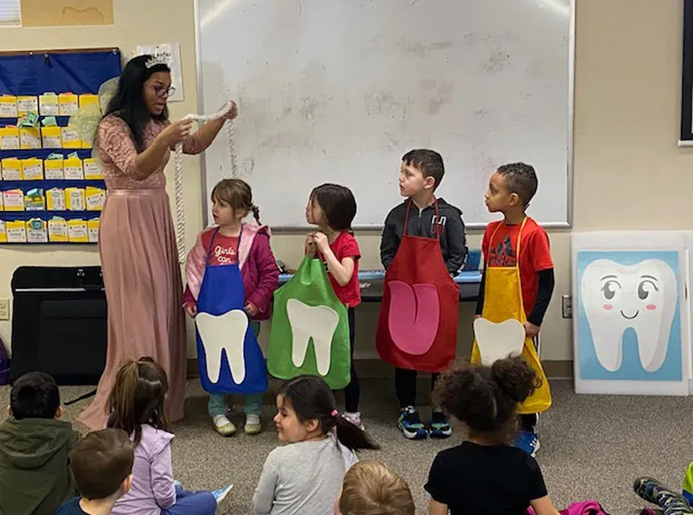 An instructor teaches children in a classroom using props of teeth and a tongue while students watch.