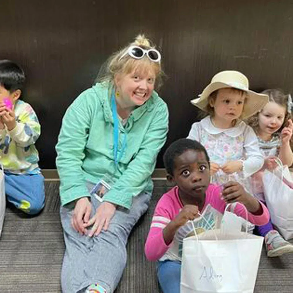An adult and four children sit on a floor holding gift bags, with one child wearing a sun hat.