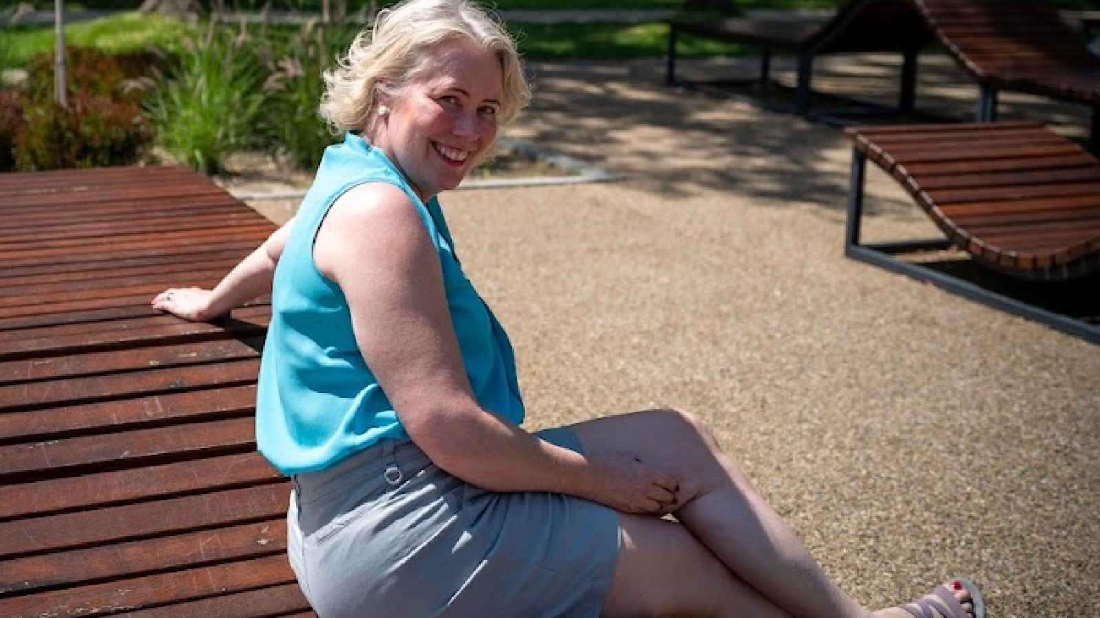 A woman is sitting on a wooden deck next to a pool.