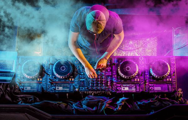 A dj is kneeling down in front of a mixer in a dark room.