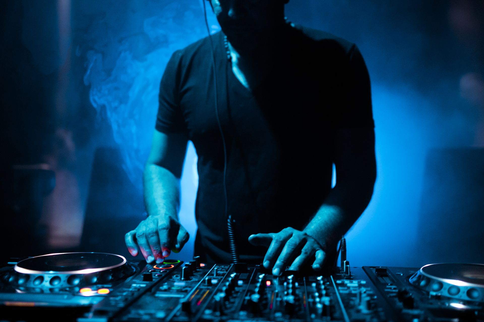A dj is playing music on a mixer in a dark room.