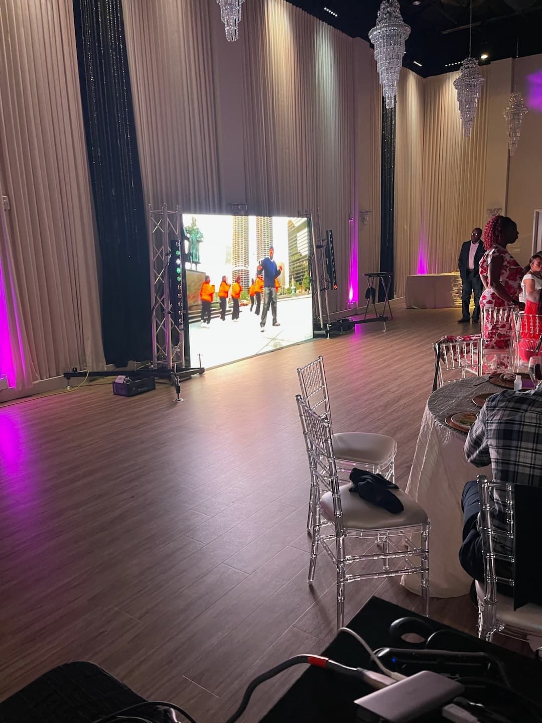 A large room with tables and chairs and a large screen on the wall.