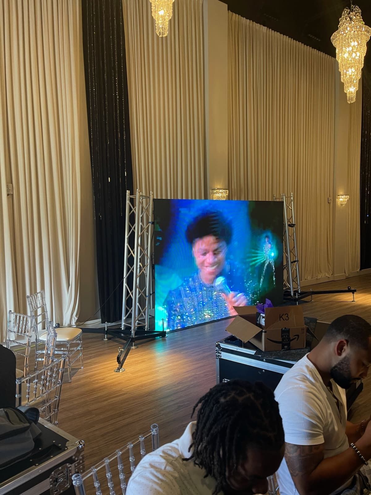 Two men are sitting in front of a large screen in a room.