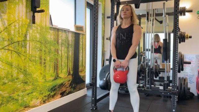 A woman is holding a kettlebell in a gym.