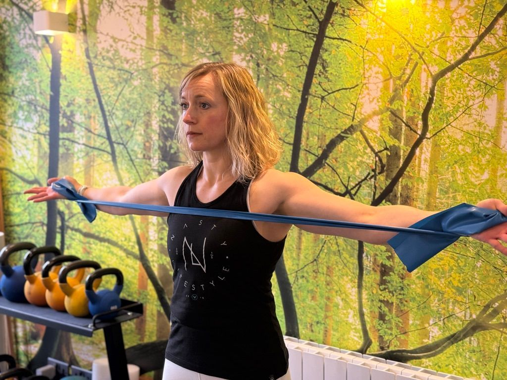 A woman is stretching her arms with a blue resistance band in a gym.