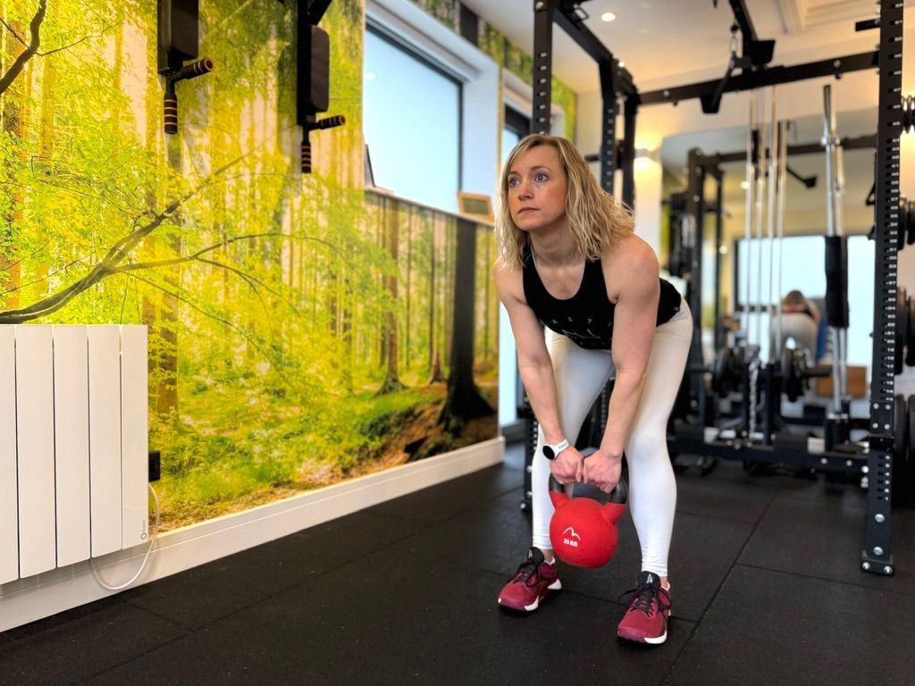 A woman is squatting down while holding a dumbbell in a gym.
