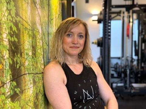 A woman is leaning against a wall in a gym.