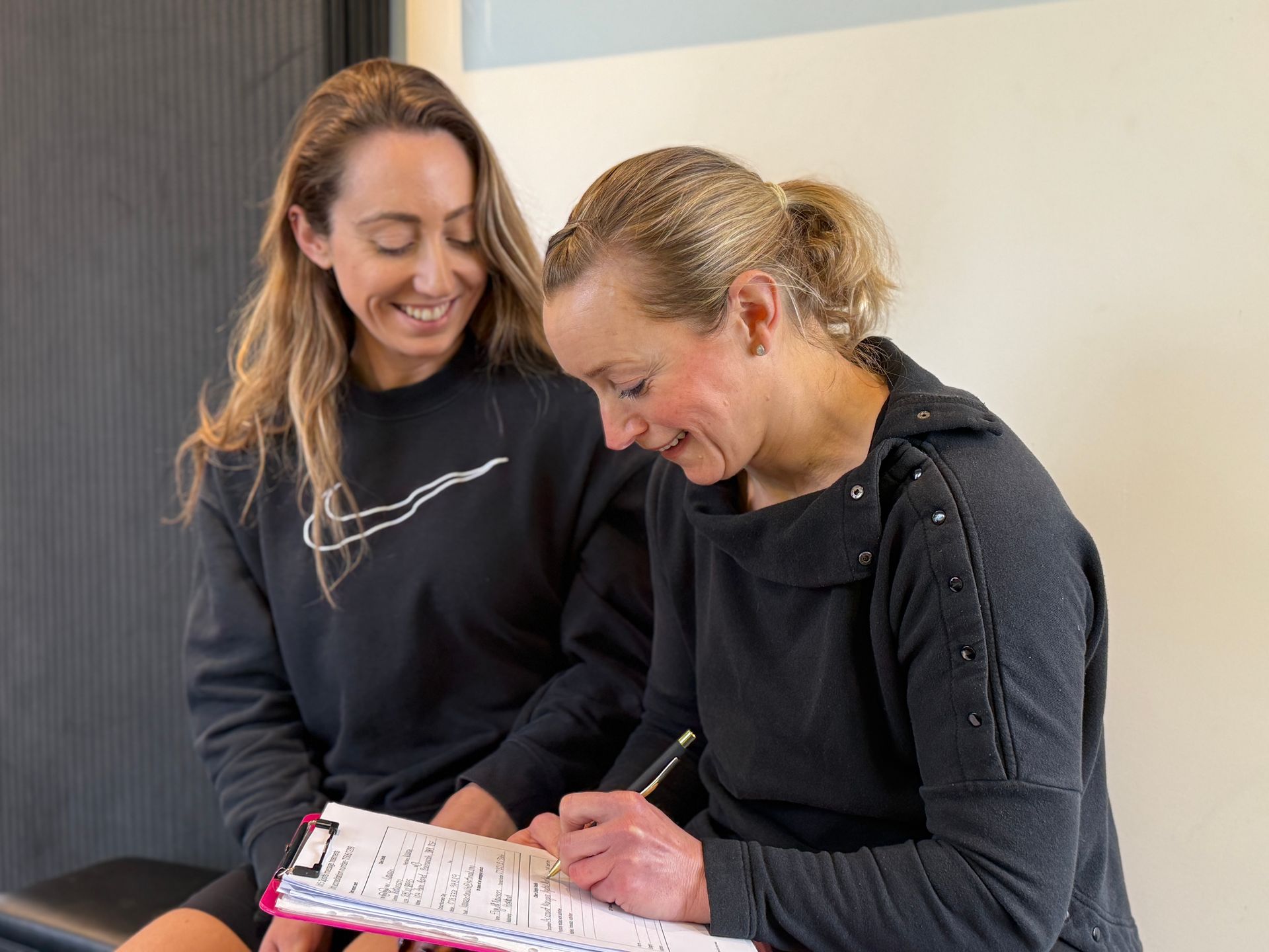 Two women are sitting next to each other looking at a clipboard.