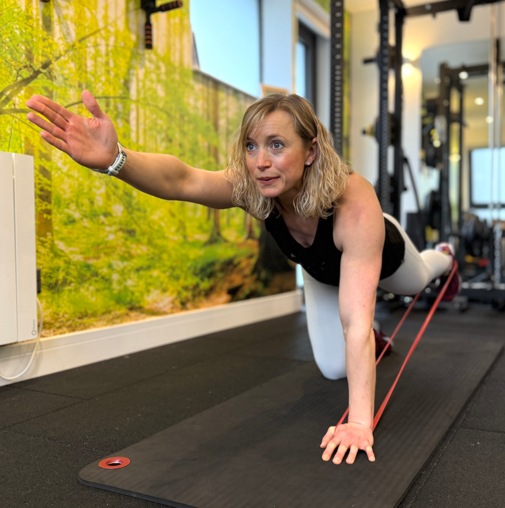 A woman is doing stretching exercises on a mat in a gym.
