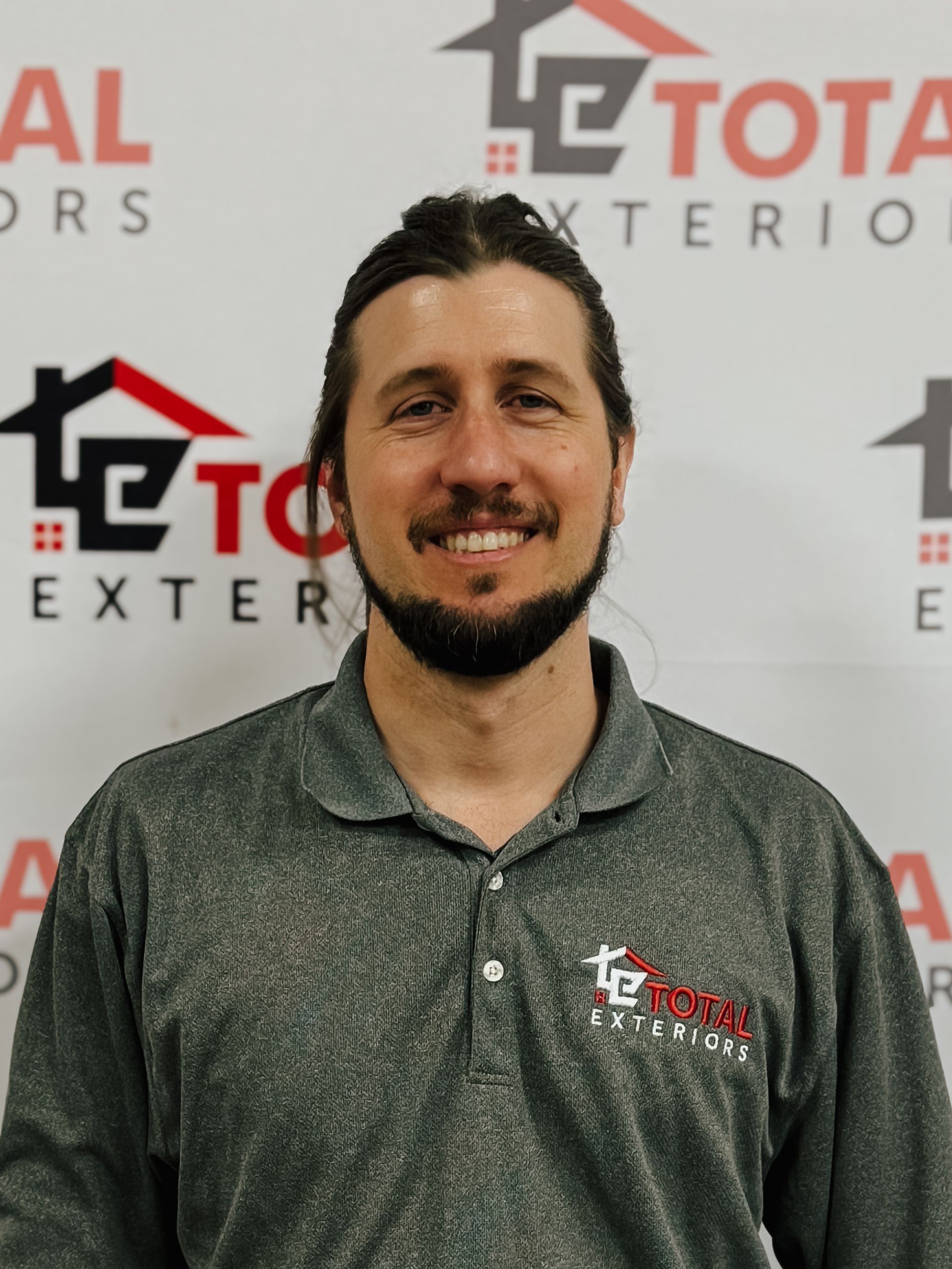 A man wearing glasses is standing in front of a wall that says total exteriors