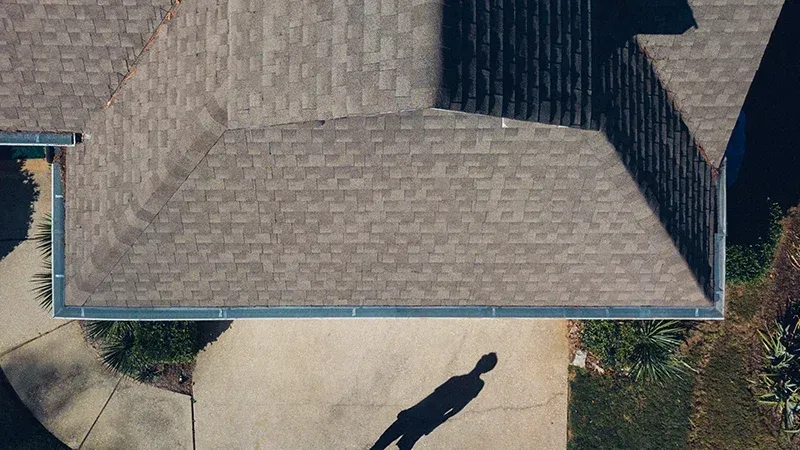 An aerial view of a house with a shadow of a person on the driveway.