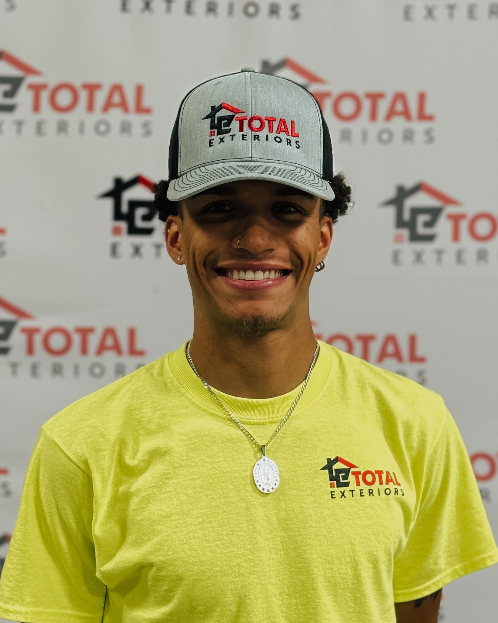 A man wearing glasses is standing in front of a wall that says total exteriors