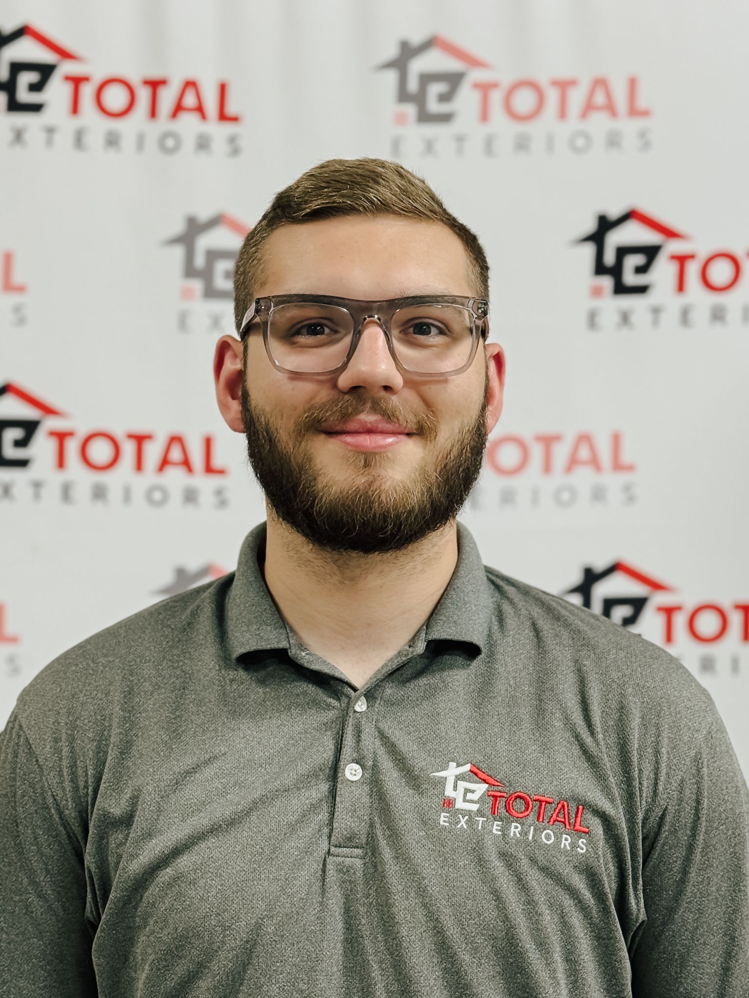 A man wearing glasses is standing in front of a wall that says total exteriors