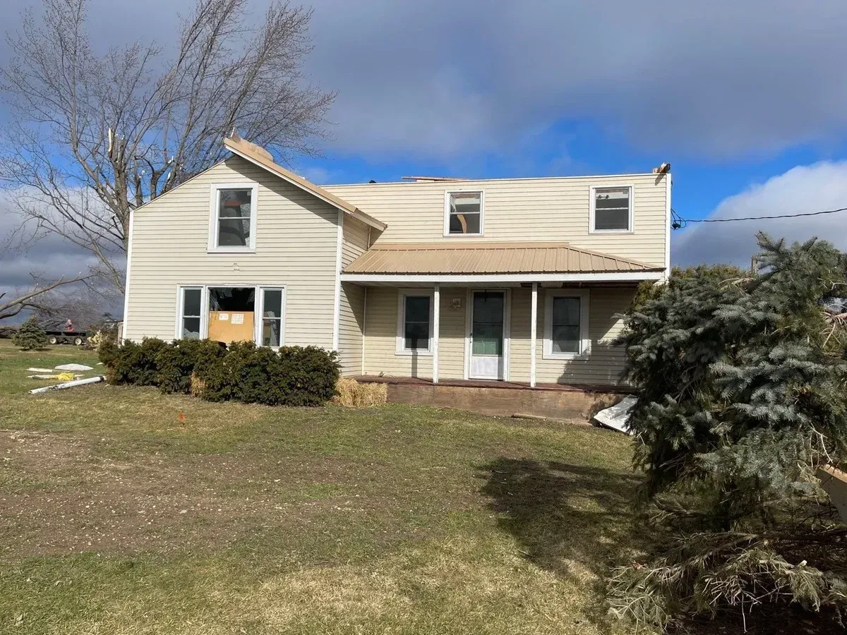 A white house with a brown roof is sitting on top of a lush green field.