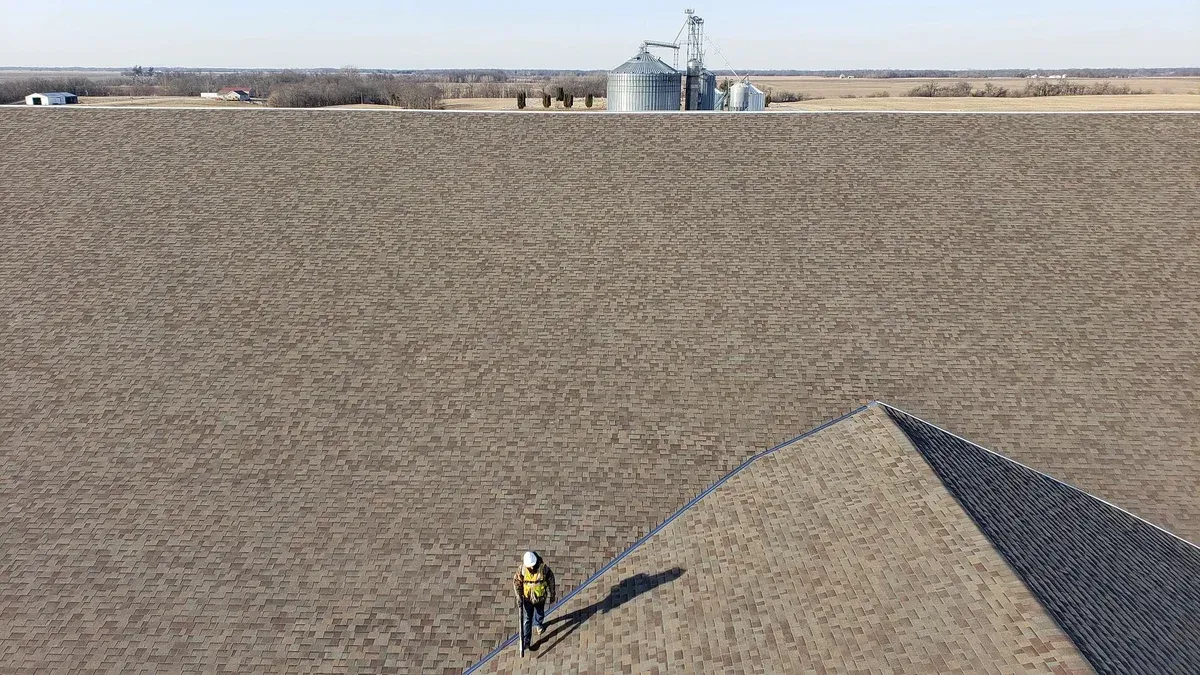 An aerial view of a man standing on top of a roof in a field.