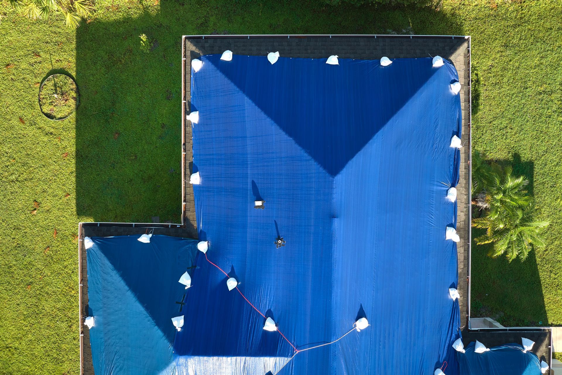 Overhead view of a blue roof with white flags and shadows on green lawn.