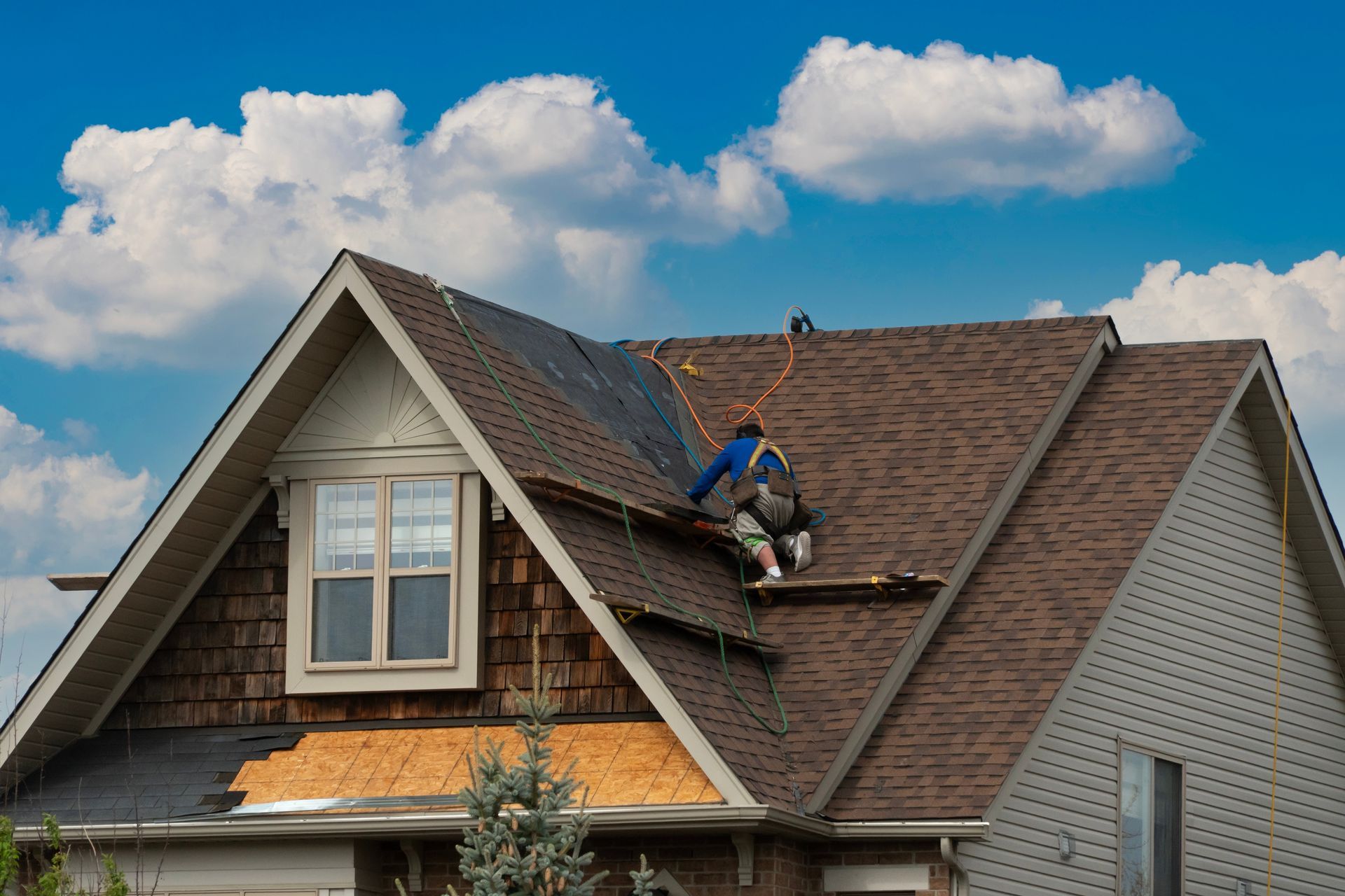 Roofer working on a brown shingle roof under a cloudy sky.