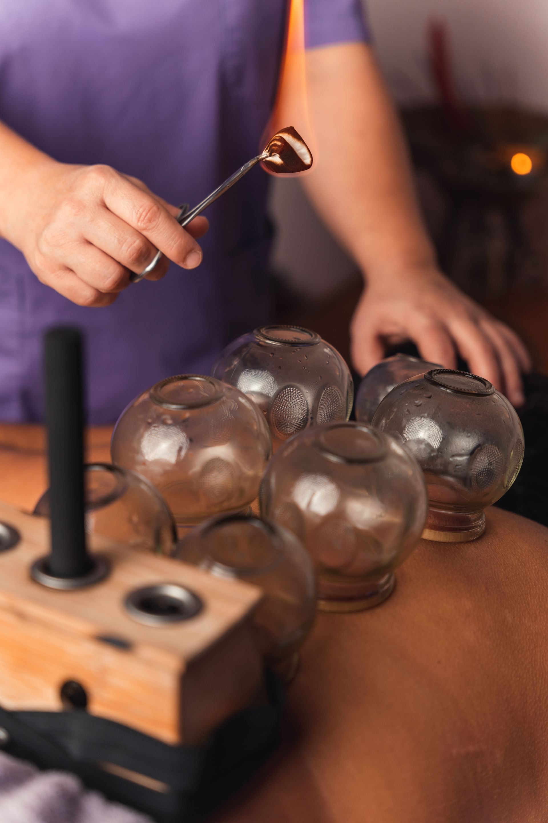 A person is holding a spoon over a bunch of glass cups on a table.