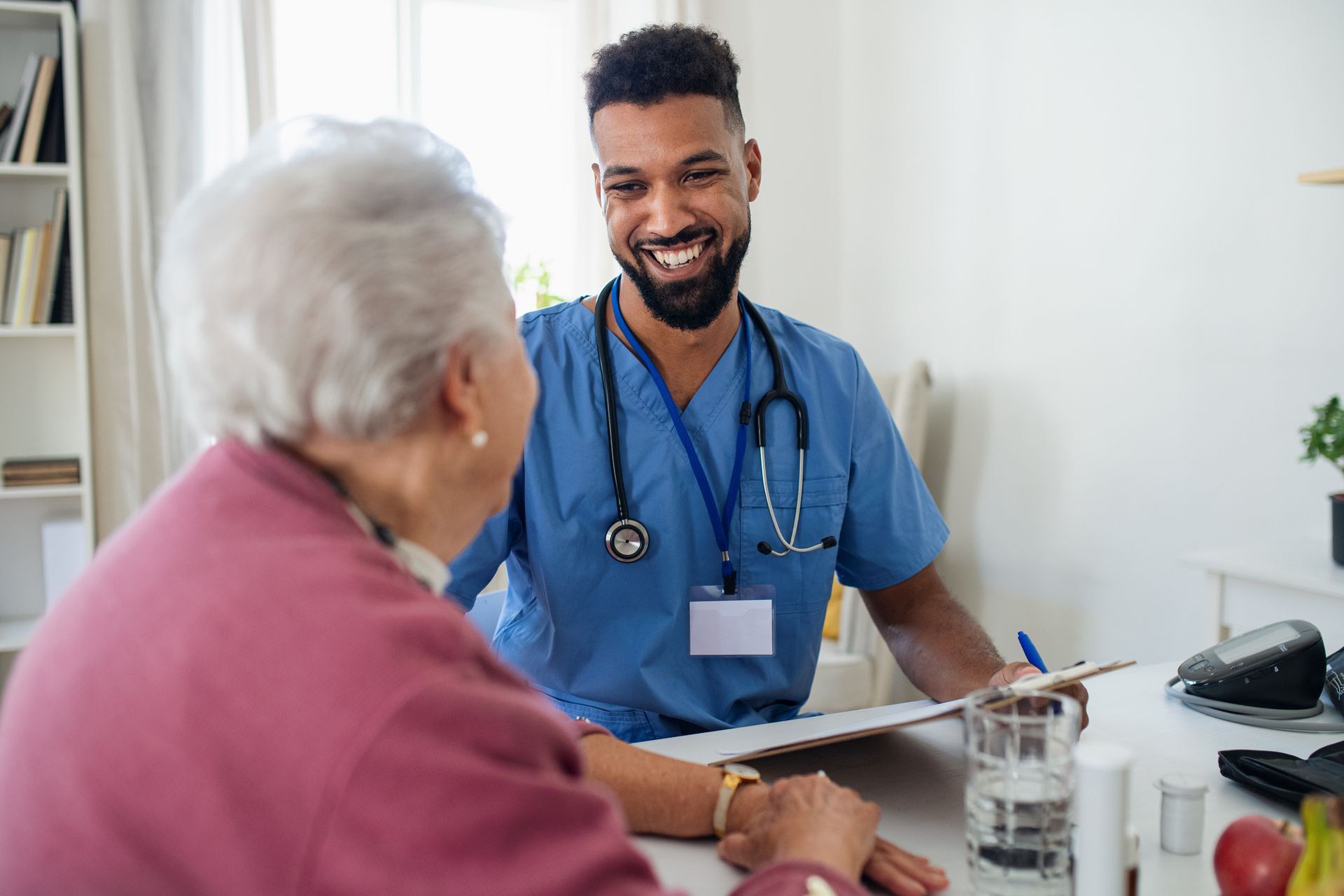 Male medical professional smiles at older patient while taking notes.