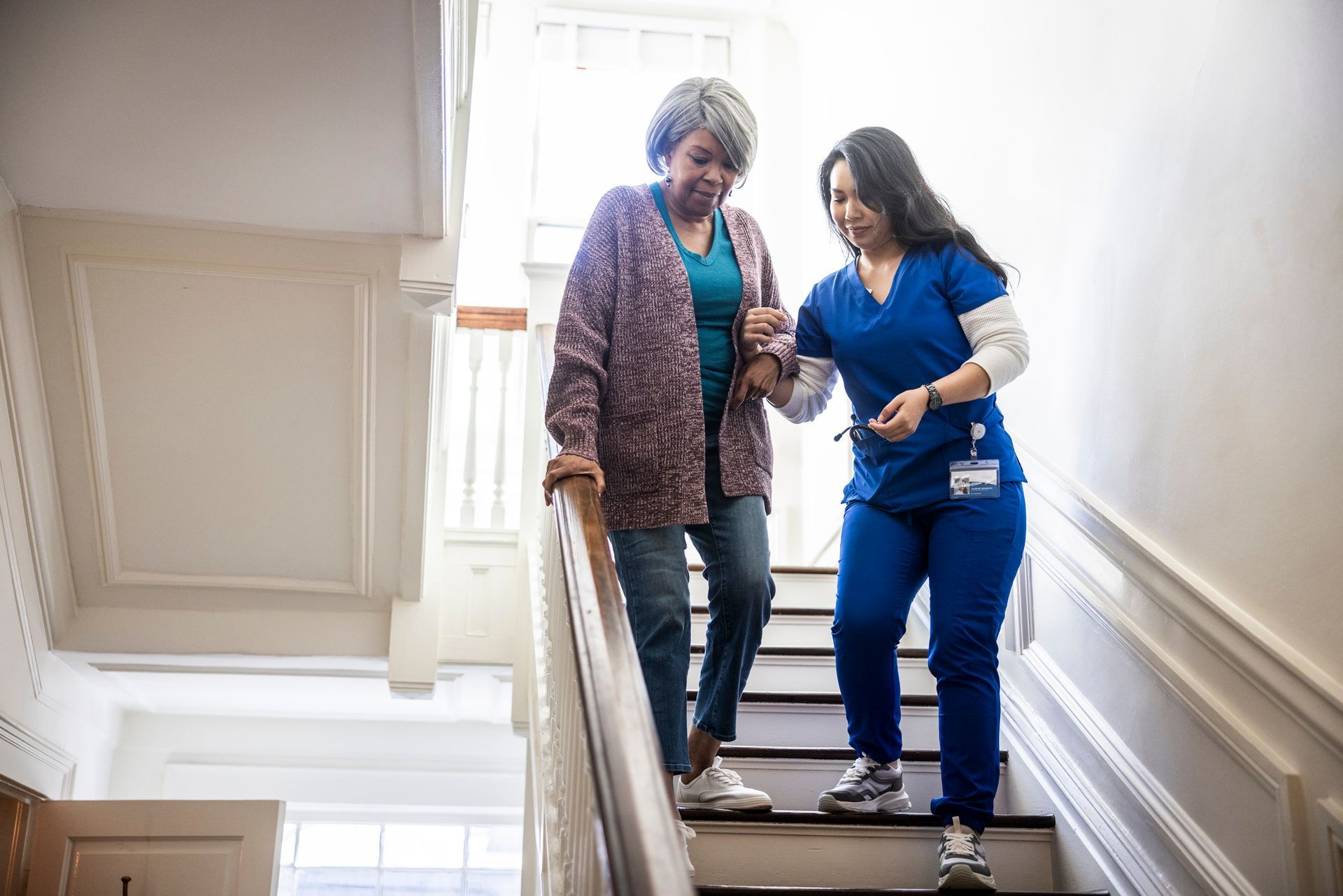 Woman with caregiver descending stairs, caregiver assisting with balance.
