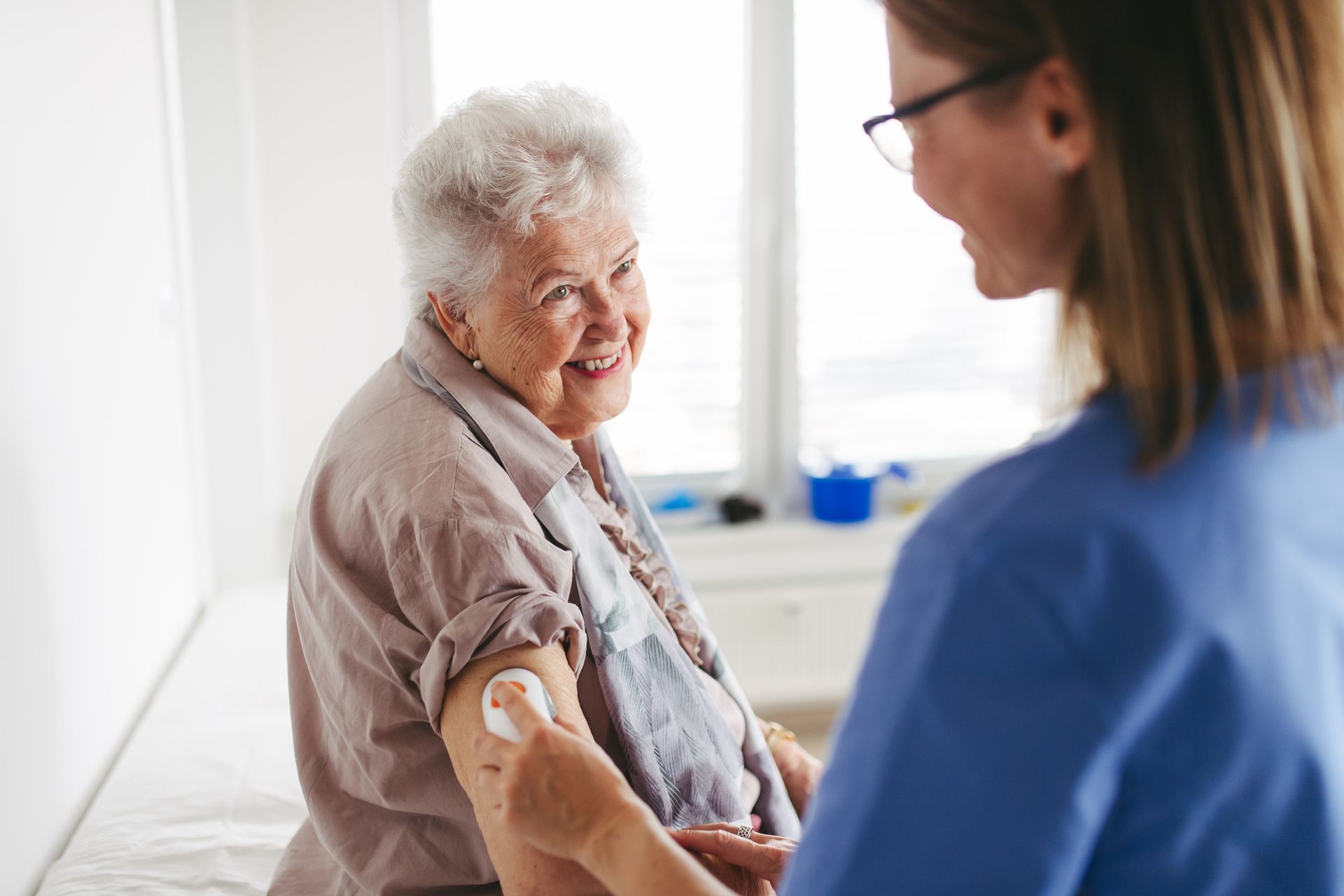 Senior woman smiles while receiving injection in arm from a medical professional. Interior shot.