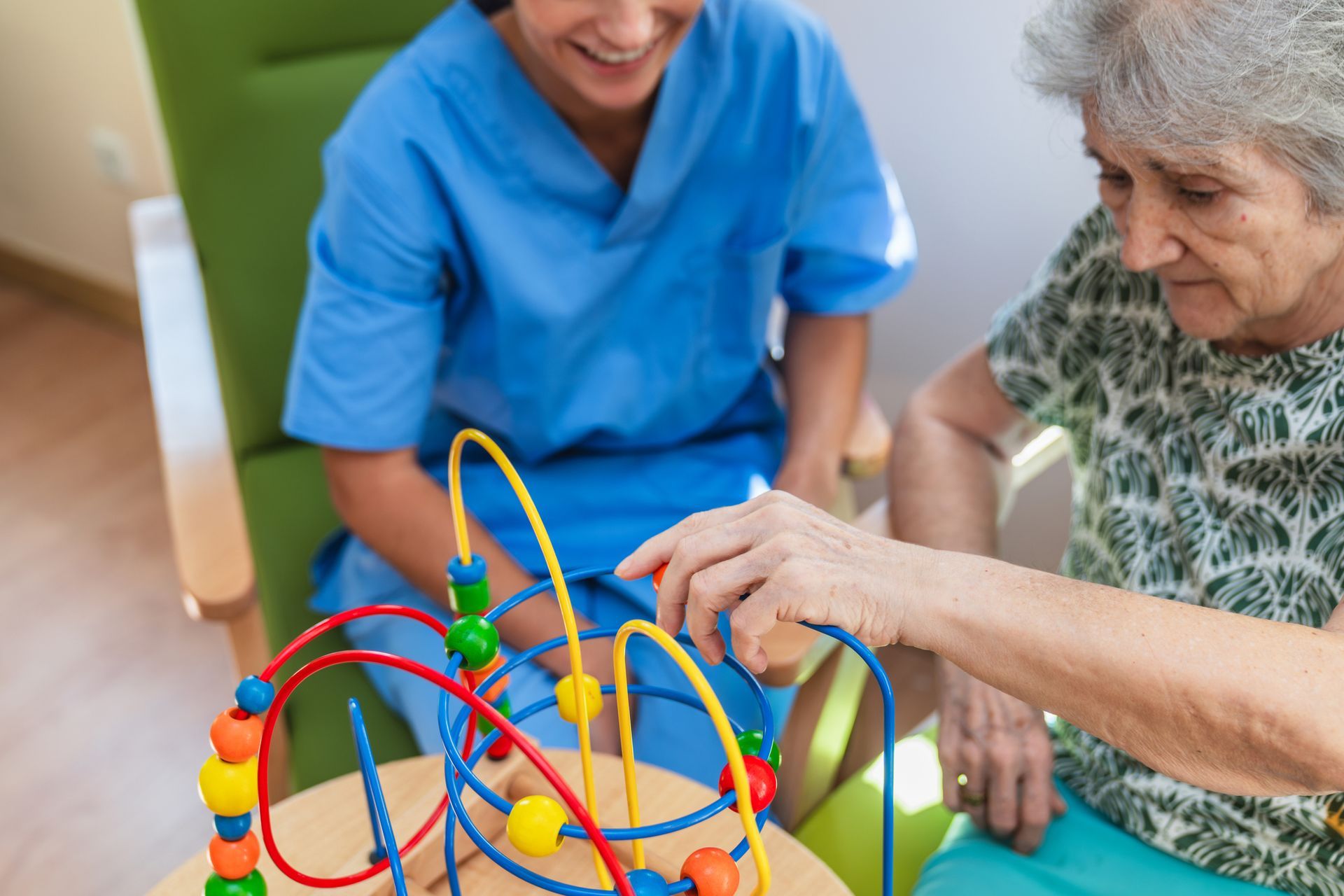 Caregiver assists elderly person with bead maze game.