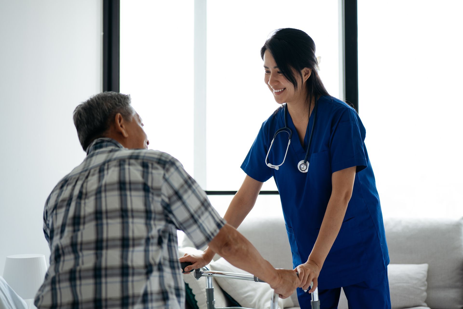 A healthcare provider helps a patient with a cane stand up indoors.