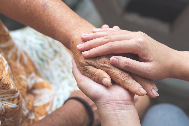 A young person's hands gently holding an older person's wrinkled hand, offering comfort.
