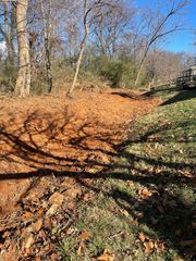 A patch of excavated, bare red earth bordered by grassy, leaf-covered ground under a clear blue sky.