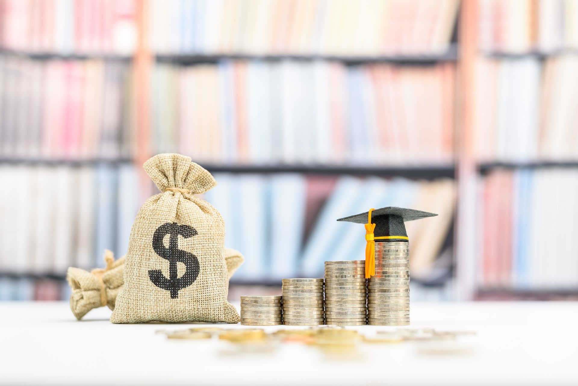 A bag of money , a graduation cap , and stacks of coins on a table.