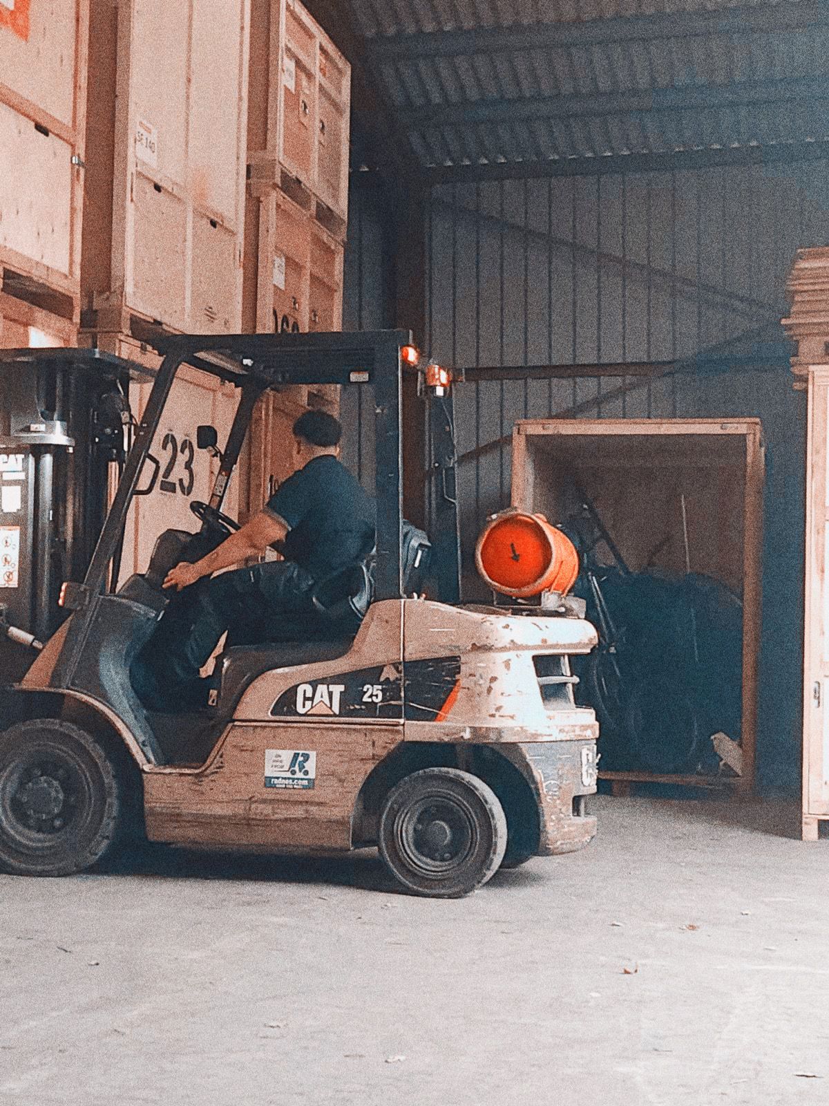 Forklift operator in a warehouse, moving wooden crates. The forklift is yellow, and the setting is dim.