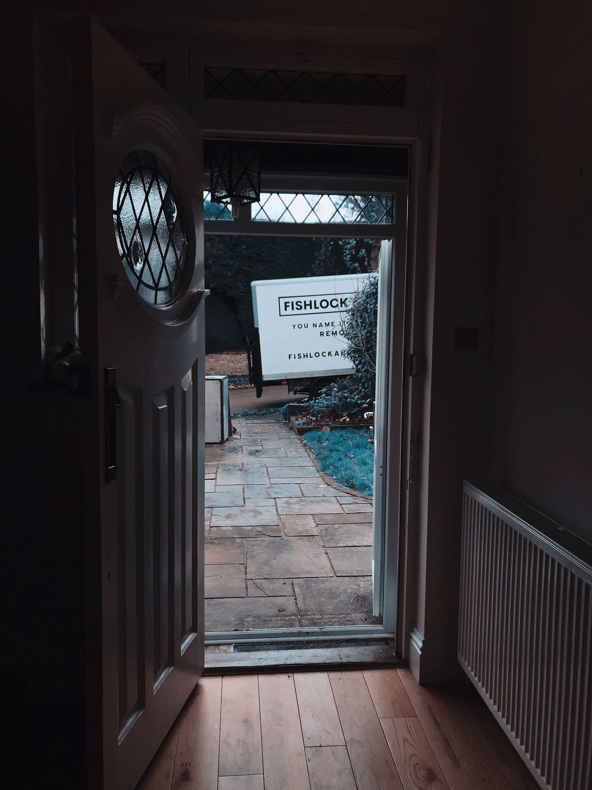 Open white front door revealing a stone pathway and a parked white van, with a view of foliage.