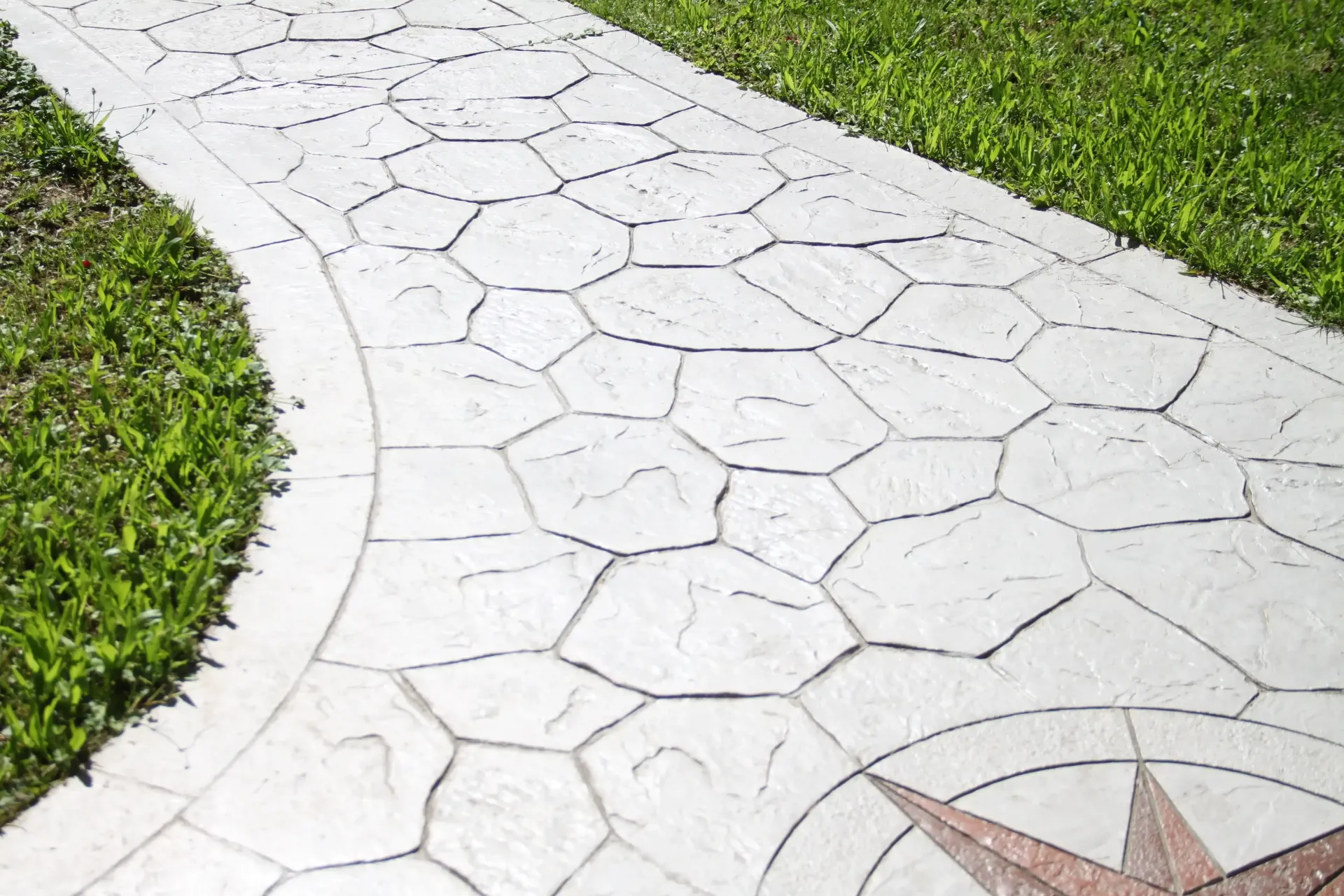 Concrete pathway with geometric stone pattern next to green grass.