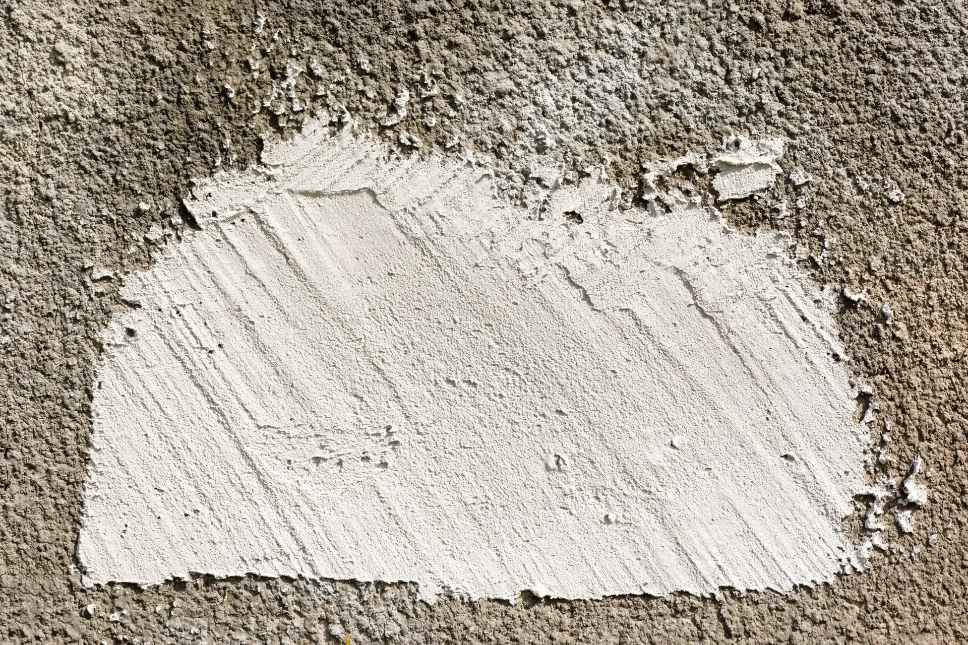 White patch of concrete on rough, gray cement wall, with visible brush strokes.