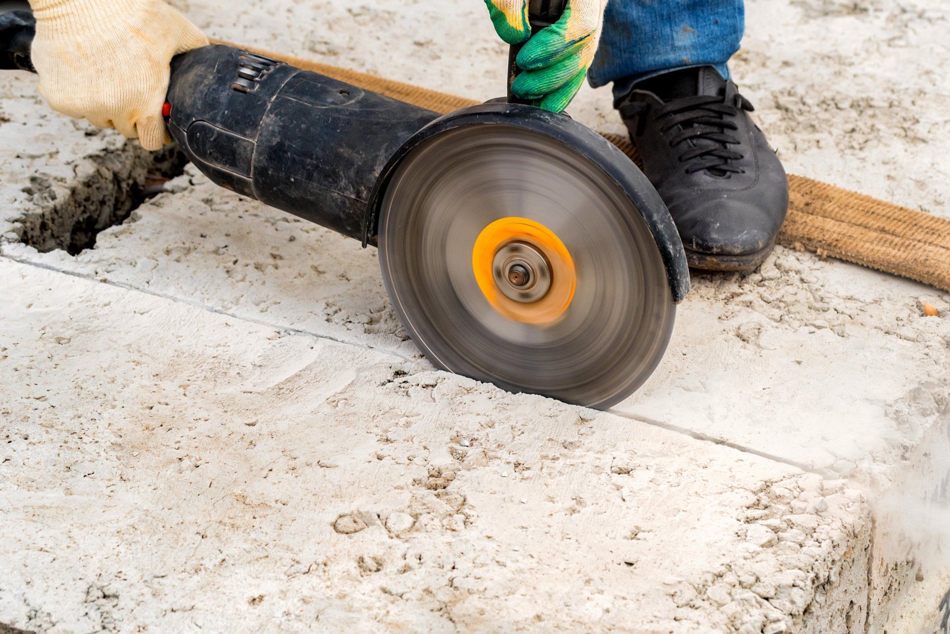 Person using an angle grinder to cut concrete, with protective gloves and shoes.