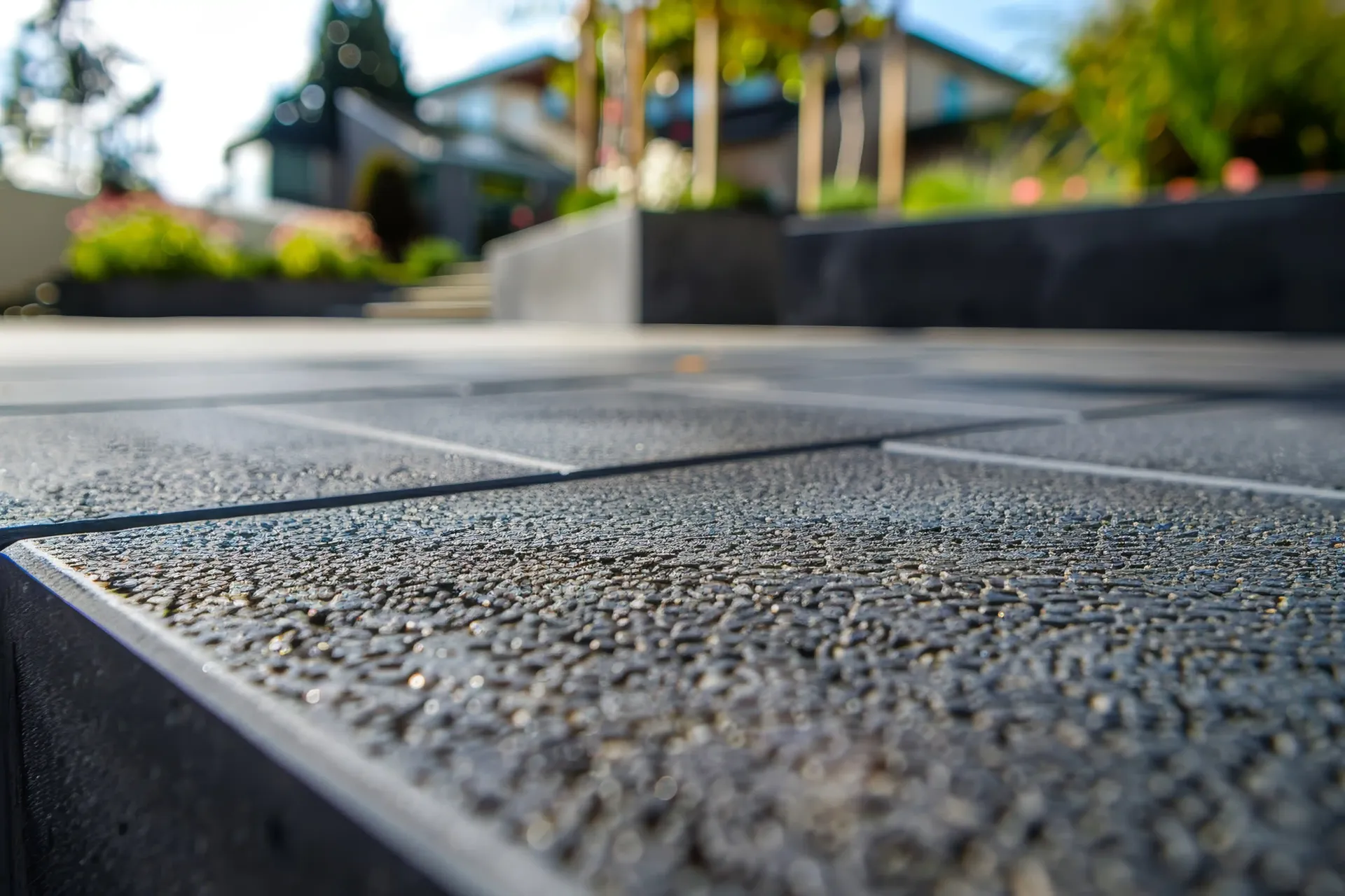 Close-up of dark gray patio stones, blurred background shows a house and trees.