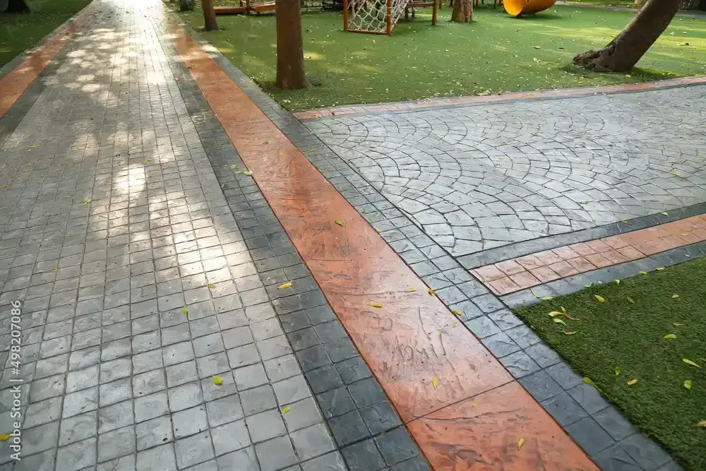 Path of patterned paving stones with orange and gray borders, leading to a playground.