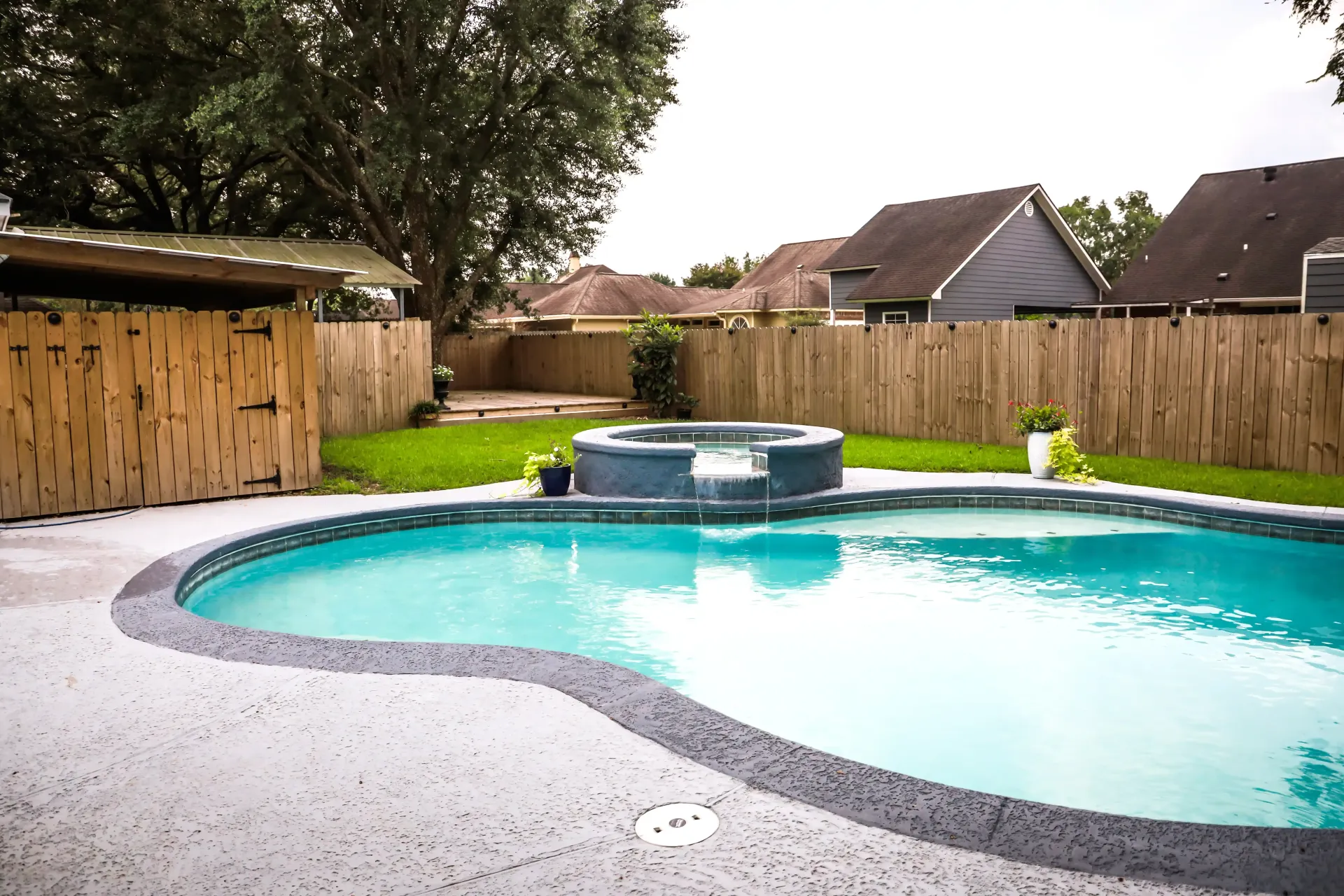 Pool with jacuzzi, wooden fence, and backyard setting.
