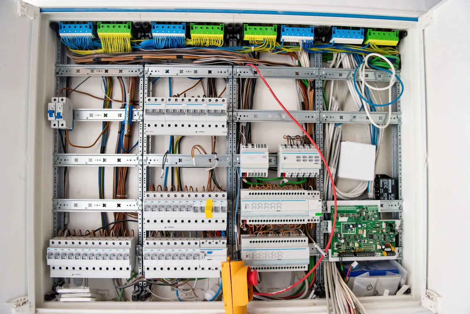 An open electrical distribution board with numerous circuit breakers, wiring, and components mounted on a metal frame.
